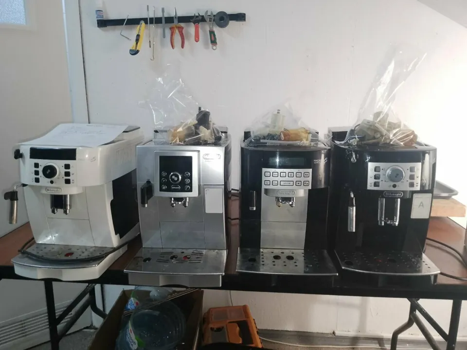 Четыре кофемашины De’Longhi на столе в мастерской, над ними инструмент на стене